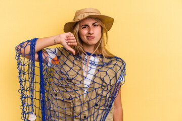 Young caucasian blonde fisherwoman holding a rod isolated on yellow background  showing a dislike gesture, thumbs down. Disagreement concept.