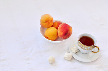 Nice cup of tea, coconut candies and peaches on the white table cloth. Copy space