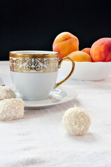Nice golden cup of tea on a plate, coconut balls and bowl of peaches