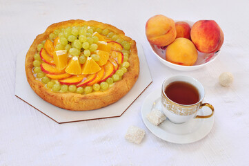 Sweet Breakfast with fruit citruc cake, fresh peaches and cup of tea on white table