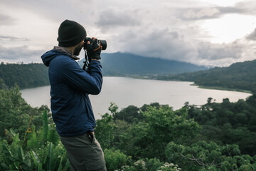 A man, a traveler, with a backpack, photographs a wild landscape.
