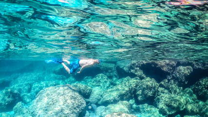 Naklejka na ściany i meble Man snorkeling in the blue sea over a rocky seabed
