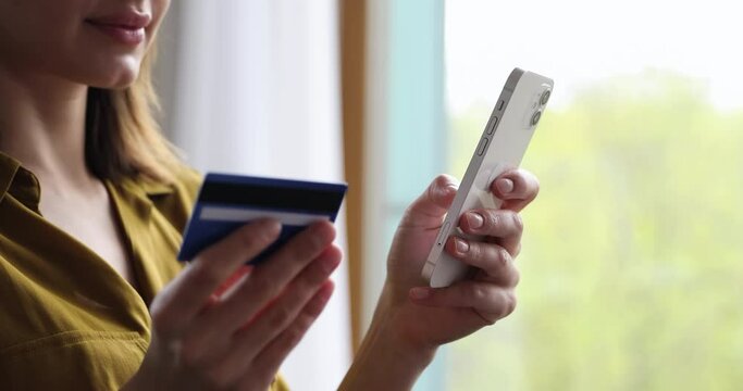Close up woman standing indoor holds debit card enters digits data makes easy comfort purchase on internet ecommerce web store. Client of electronic services, distance shopping, secure payment concept