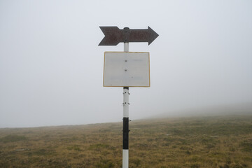 Old and rusty blank hiking sign posts, marking hiking routes up on the mountain on a foggy day.