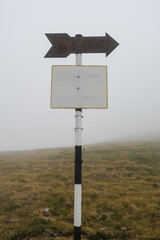 Old and rusty blank hiking sign posts, marking hiking routes up on the mountain on a foggy day.