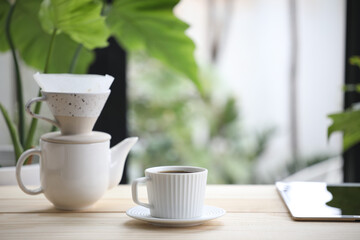 White coffee cup and ceramic coffee drip pot and tablet on wooden desk