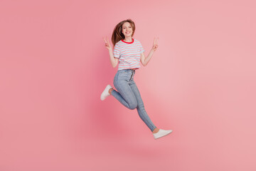 Fototapeta na wymiar Portrait of cheerful carefree lady jump run have fun show v-signs on pink background