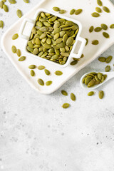 Pumpkin seeds in a white bowl on a light gray culinary background top view from a copyspace