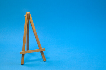 Small empty easel on bright blue background, close up with copy space