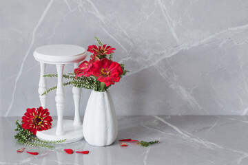 red flowers in white vase and wooden stand on gray marble background