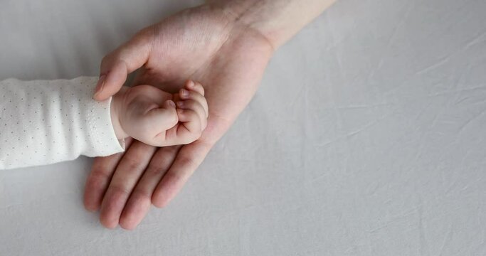 Close up above view loving mommy holds hand of her newborn while baby sleeping lying on bed during healthy day nap. Cherish, mothers love and care, protection of children, adoption, babyhood concept