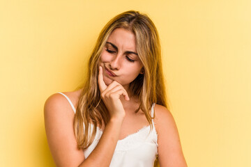 Young caucasian blonde woman isolated on yellow background  looking sideways with doubtful and skeptical expression.