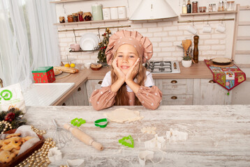 a little girl folded her hands on a table under her chin in the home kitchen around her flour with room for text.