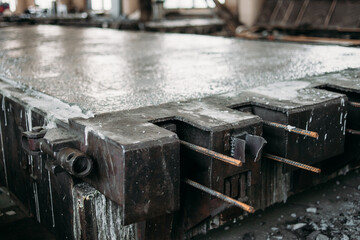 A loaded concrete-filled metal mold for the production of a reinforced concrete road slab is located in the workshop of a reinforced concrete plant.