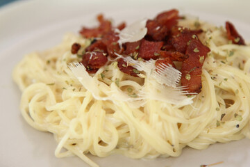 Spaghetti carbonara with cheese and crispy bacon on white plate.