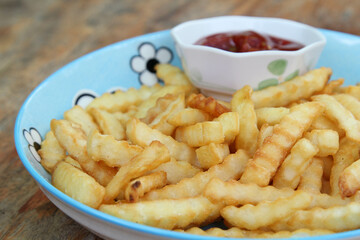 Delicious french fries with ketchup in ceramic plate on wooden table.