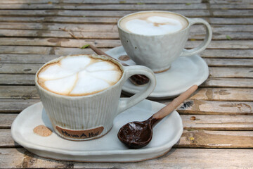 Hot coffee cappuccino in white ceramic cup and spoon on bamboo table.