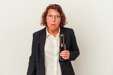 Middle age latin business woman holding a beer isolated on white background shrugs shoulders and...