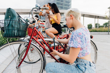 Young caucasian woman fastening bicycle using padlock outdoors