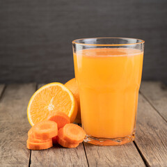 Orange and carrot juice in a glass with fruits over wooden table