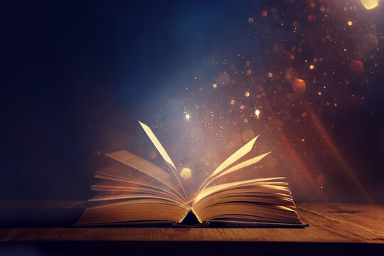 Magical image of open antique book over wooden table with glitter lights