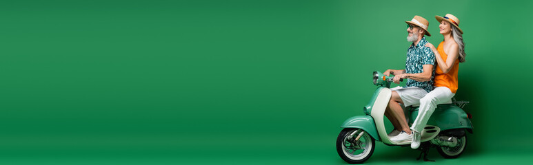 cheerful interracial and middle aged couple in sun hats riding moped on green, banner © LIGHTFIELD STUDIOS