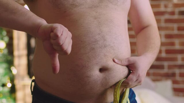 Fat man gropes his stomach and shows dislike to the camera. Overweight man touches his belly and gives thumbs down. Concept of unhealthy lifestyle