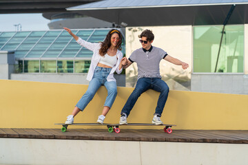 Cheerful hipster man and woman young couple having fun after skateboarding laugh enjoy time outdoors together. Carefree male and female skaters joyful relax on longboard. Freedom and lifestyle concept