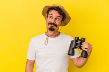 Young caucasian man holding binoculars isolated on yellow background dreaming of achieving goals and purposes