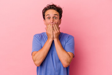 Young caucasian man isolated on pink background shocked covering mouth with hands.