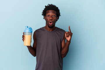 Young african american man holding protein milkshake isolated on blue background having some great idea, concept of creativity.