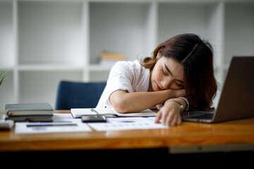 Young tired woman with laptop sleeping on desk at work in office