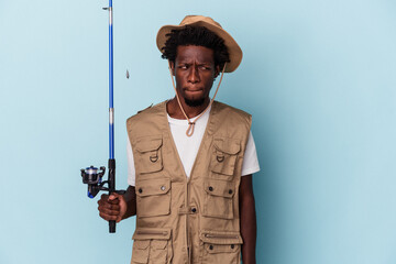 Young african american fisherman holding a rod isolated on blue background confused, feels doubtful and unsure.