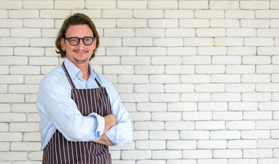 Portrait of happy senior man gardening wearing glasses and denim apron standing in front of white brick on background with free space or copy space for text. looking at camera.