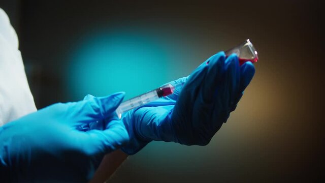 Doctor filling syringe with red solution. Nurse wearing protective gloves showing sample of medicine, vaccination against covid-19, laboratory research concept. Coronavirus vaccine.