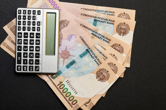 Uzbek money and calculator on black. Pile of Uzbek sums and calculator. Concept of exchange rate. Economic or financial concept