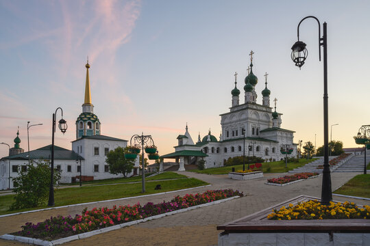 Ancient majestic churches with old bells and green-gold domes on the central square in the provincial town of Solikamsk (Northern Ural, Russia) in summer. Brick patterned masonry walls, flower beds