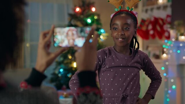 christmas funny african american girl wearing reindeer antlers posing for mother taking photos using smartphone having fun enjoying festive holiday memories at home 4k 