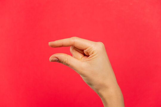 Mano se&ntilde;al de algo peque&ntilde;o, fondo rojo.