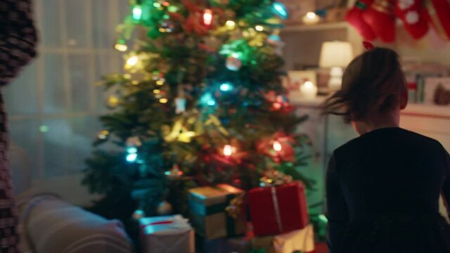 happy little girl putting presents under christmas tree smiling excited for festive holiday enjoying celebrating with family and friends 4k