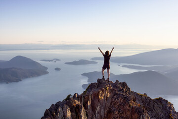 Adventurous Caucasian Woman Hiking on top of a Rocky Mountain Cliff. Sunny Summer Sunset. Mnt...