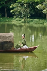 Foto op Canvas Happy beautiful young Asian woman in tradtional costume sitting in boat and looking at camera © DragonImages