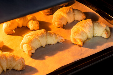 Oven-baked croissants on baking sheet with parchment paper. Sweet bagels baked in hot oven. The process of making curd bagels or croissants
