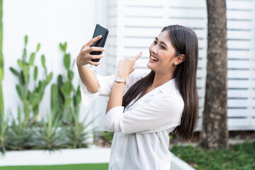 Asian young businesswoman in wear casual saying hi to the mobile camera during using smart phone video call while standing near the business office.