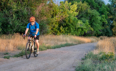 senior male cyclist is riding a touring bike on a gravel trail at Colorado foothills, late summer...