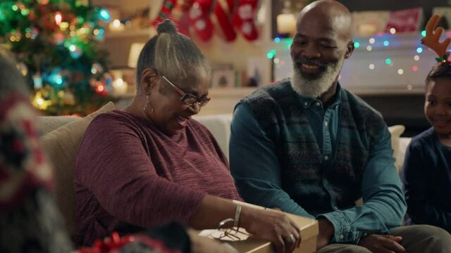 african american grandmother opening christmas gift with surprise sexy bra laughing enjoying funny joke with family celebrating festive holiday at home 4k