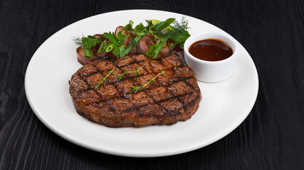 Grilled black angus steak ribeye on white plate on black wooden background