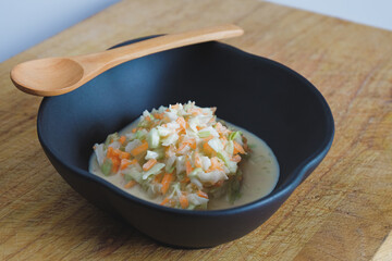Coleslaw salad in black bowl on wood cutting board background.