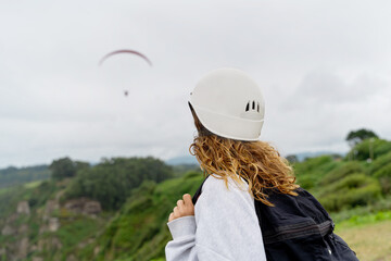Side view of unrecognizable woman with helmet and paragliding equipment outdoors. Panoramic view of adventurous woman practicing risky sports. Adventure and sport lifestyle.