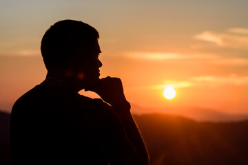 Man with hands on chin stand on the mountain and watching over the misty sunset